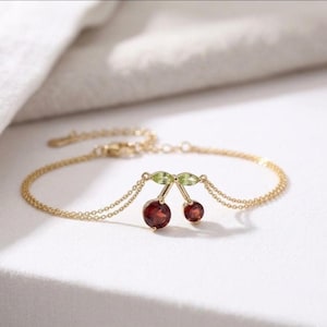 May include: Gold bracelet with a cherry pendant. The cherries are a deep red colour, with green leaves. The bracelet has a delicate chain and a lobster clasp. A charming piece of jewellery.