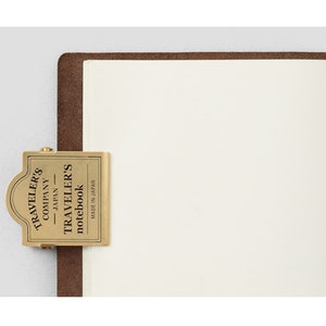 Op de afbeelding: Een messing notitieboekclip van Traveler's Company met de tekst "Traveler's Company Japan Traveler's notebook Made in Japan" erop.