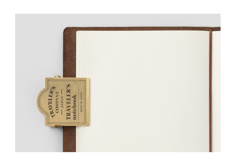 Op de afbeelding: Een messing notitieboekclip van Traveler's Company met de tekst "Traveler's Company Japan Traveler's notebook Made in Japan" erop.