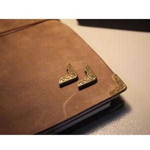 Peut inclure: Un journal relié en cuir marron avec des coins décoratifs en laiton. Le journal a un aspect usé et vintage.
