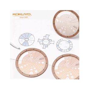 Puede incluir: Un conjunto de cuatro plantillas circulares marrones y transparentes con varias formas geométricas y recortes. Las plantillas están sobre un fondo blanco con diagramas dibujados a mano y el texto "KOKUYO since 1905". También se ve un bolígrafo.