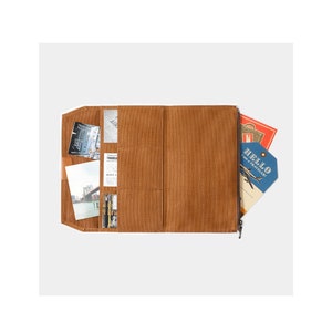 May include: A brown leather zippered travel wallet with multiple pockets and slots for cards, cash, and other travel essentials. The wallet is open and has various cards and travel tickets inside.