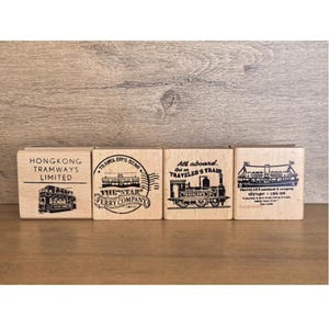 May include: Four rectangular wooden stamps featuring black ink illustrations and text. The stamps depict a Hong Kong tram, a Star Ferry Company logo, a steam locomotive with the text All aboard Traveler's Train, and a ferry boat illustration.