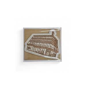 May include: Embroidered patch featuring a detailed brown and beige building design. The patch is in a clear plastic sleeve, resting on a brown card. The building has multiple stories and a unique architectural style, likely a historical landmark.
