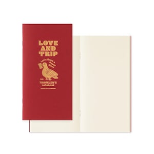 May include: A red Traveler's Notebook with gold lettering reading "LOVE AND TRIP". The cover displays a gold dove illustration with a flag, and the text "Let's Draw a Peace Dove" and "TRAVELER'S notebook" below the dove.