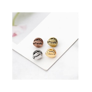 Puede incluir: Cuatro abalorios de grano de café en diferentes acabados metálicos: plata, oro rosa, oro y bronce. Los abalorios son pequeños y detallados, con un diseño realista de grano de café.