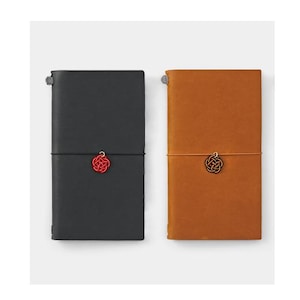May include: Two leather-bound notebooks with a red and black string closure. Each notebook has a small red and black tassel charm.