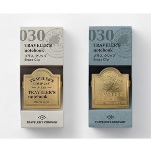 Op de afbeelding: Twee dozen met messingclips voor Traveler's notitieboekjes. De dozen zijn wit en blauw met de tekst "030 Traveler's notebook Brass Clip" op de voorkant. De messingclips hebben de tekst "Traveler's Company Japan Traveler's notebook" erop.
