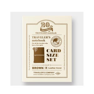 May include: A cream-colored card set for a Traveler's Notebook. The front features text that reads "20th Anniversary Traveler's Notebook" and "Card Size Set." The set includes a brown leather cover. The text "Brown / Leather Cover" is also visible.