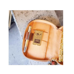 May include: A light brown leather organiser with a gold zip, pen, and a decorative ticket that reads "PARTY SPECIAL EVENT". The organiser has multiple pockets and gold-coloured metal rings.
