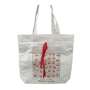 Può includere: Borsa tote in tela bianca con manici in nastro rosso. La borsa presenta un motivo ripetuto di personaggi di Babbo Natale con il testo "HAPPY NEW YEAR" e "MERRY CHRISTMAS". La parte inferiore della borsa ha il testo "MANUAL FACTORY AYES X LOG-ON".