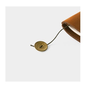 May include: A brown leather-bound notebook with a brass closure and a black string tie.