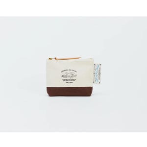 Puede incluir: Pequeño neceser rectangular de lona con base marrón y parte superior color crema. El neceser tiene una cremallera dorada y una lengüeta de cuero. El texto "STANDARD AND STRONG SUPERIOR LABOR" está impreso en la parte delantera. Una pequeña etiqueta está adjunta al lateral.