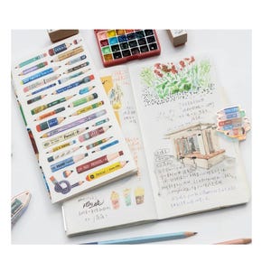 Könnte beinhalten: Ein offenes Notizbuch mit einer Aquarell-Illustration eines Gebäudes und Blumen. Das Notizbuch hat eine Seite mit bunten Bleistift-Illustrationen und dem Text "Pencil - Japan" darauf. Das Notizbuch ist auf einer Seite mit einer Aquarell-Illustration eines Gebäudes und Blumen geöffnet. Das Notizbuch hat eine Seite mit bunten Bleistift-Illustrationen und dem Text "Pencil - Japan" darauf.