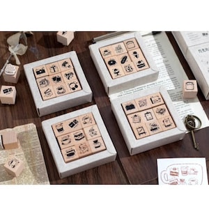 May include: Set of nine wooden stamps with various designs, including coffee cups, cakes, and other food items. The stamps are arranged in a grid pattern on a wooden surface.