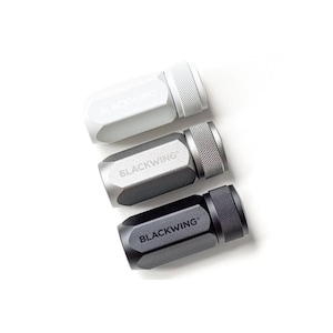 Op de afbeelding: Drie zeshoekige puntenslijpers in wit, zilver en zwart, elk met een getextureerde zilveren grip en het "BLACKWING" logo. De slijpers zijn gerangschikt op een witte achtergrond.