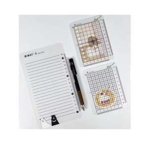 May include: A set of three clear plastic stationery items, including a lined notepad with bear illustrations and two grid rulers. A black and brown pen is also included. The notepad has the text "IMAT".