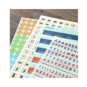 May include: Sticker sheets featuring various designs and text. Includes orange and green circle stickers, icons, letters, numbers, and months like January and June. The words "LARGE SIZE" are also visible.