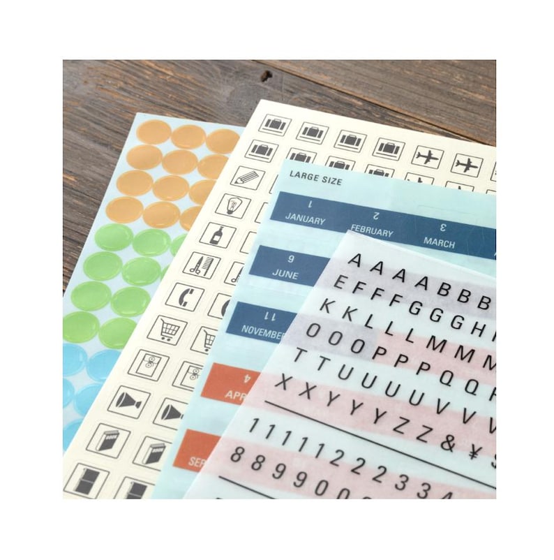 May include: Sticker sheets featuring various designs and text. Includes orange and green circle stickers, icons, letters, numbers, and months like January and June. The words "LARGE SIZE" are also visible.