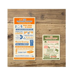 May include: Two rectangular travel-themed cards with text and illustrations. The larger card has an orange top and blue text, including phrases like "Analog Lovers" and "A Road Trip!" The smaller card is green with similar text.