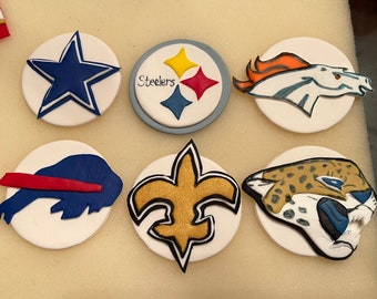 May include: A collection of white, circular decorations featuring various team logos. Logos include a blue star, a Steelers logo with the word "Steelers", a horse head, a buffalo, a fleur-de-lis, and a jaguar head.