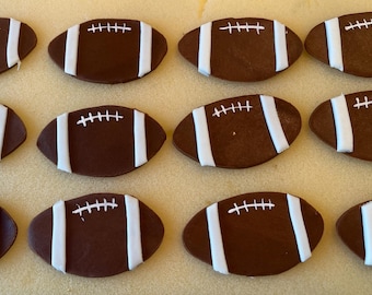 May include: Twelve brown and white football-shaped cookies with white icing and stitching details.