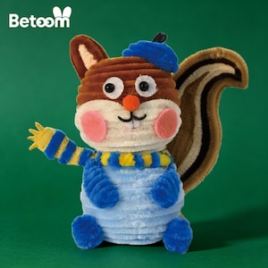 Op de afbeelding: Een handgemaakt eekhoornfiguur gemaakt van chenilledraad. De eekhoorn heeft een bruin lichaam, een blauwe baret en een blauw-gele gestreepte sjaal. De achtergrond is groen. Het woord "Betoom" staat linksboven.
