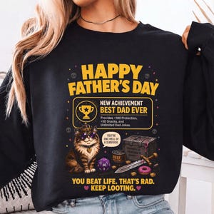 May include: Black sweatshirt with a graphic that reads "HAPPY FATHER'S DAY" and "BEST DAD EVER." The design includes a cat wearing sunglasses, a treasure chest, a sword, and a donut. The text also says "YOU BEAT LIFE. THAT'S RAD."