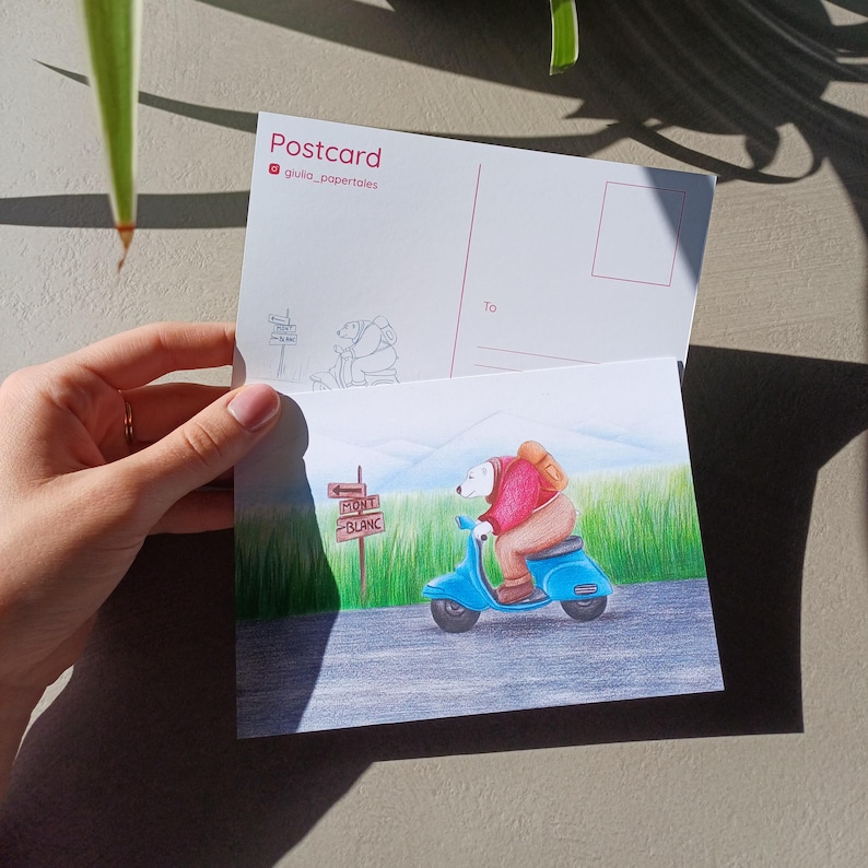 Może przedstawiać: Poczt&oacute;wka z zabawną ilustracją niedźwiedzia polarnego jadącego na niebieskim skuterze w kierunku znaku z napisem "Mont Blanc". Niedźwiedź ma na sobie czerwoną kurtkę i plecak. Poczt&oacute;wka jest oznaczona "Postcard" z nazwiskiem artysty.