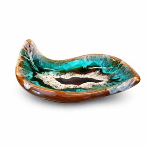 May include: A ceramic, leaf-shaped dish with a glossy finish. The dish features a brown rim and a vibrant interior with shades of turquoise, white, and dark brown. The design is reminiscent of a flowing, abstract pattern.