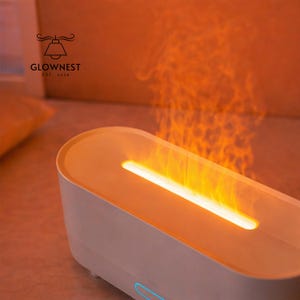May include: A white and orange electric fireplace with a flame effect. The product has a rectangular shape with rounded edges and a glowing orange light emanating from the top. The brand name "GLOWNNEST" is visible in the upper left corner.