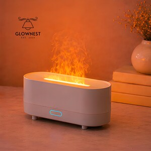 May include: A white oval aromatherapy diffuser with a flame effect. The diffuser has a blue light and the text "GLOWNNEST EST. 2020". The flame effect emits orange and yellow light.
