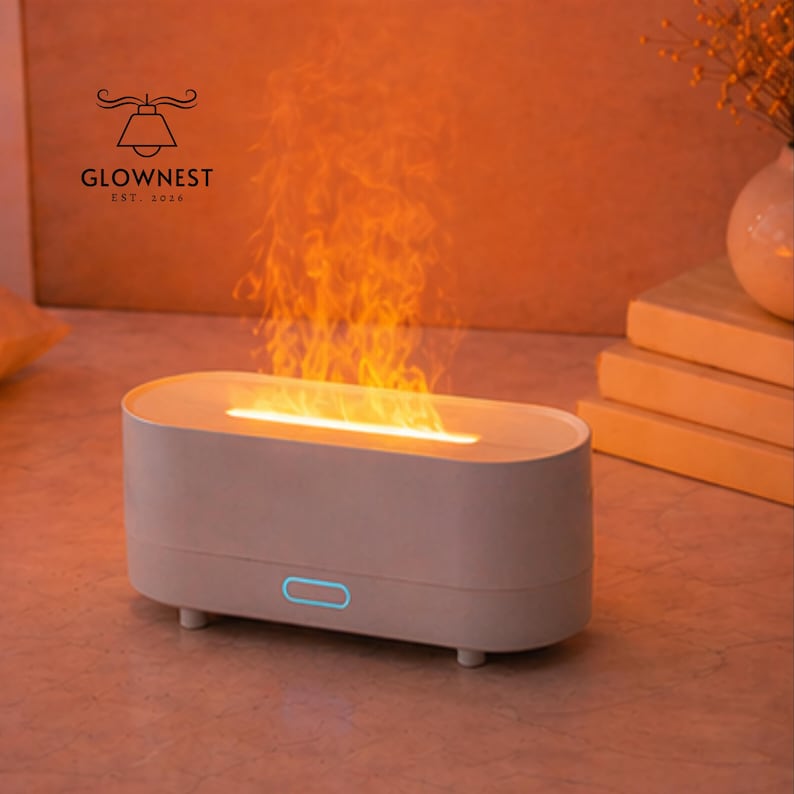 May include: A light grey, oval aromatherapy diffuser with a flame effect. The diffuser has a blue light and is branded "GLOWNNEST EST. 2016". The flame effect emits an orange glow, creating a warm ambiance.