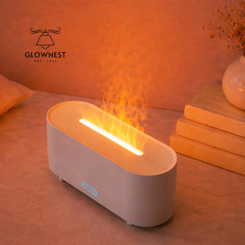 May include: A white, oval aromatherapy diffuser with a flame effect. The diffuser has a glowing light and a blue power indicator. The logo "GLOWNNEST EST. 2016" is visible on the top left.