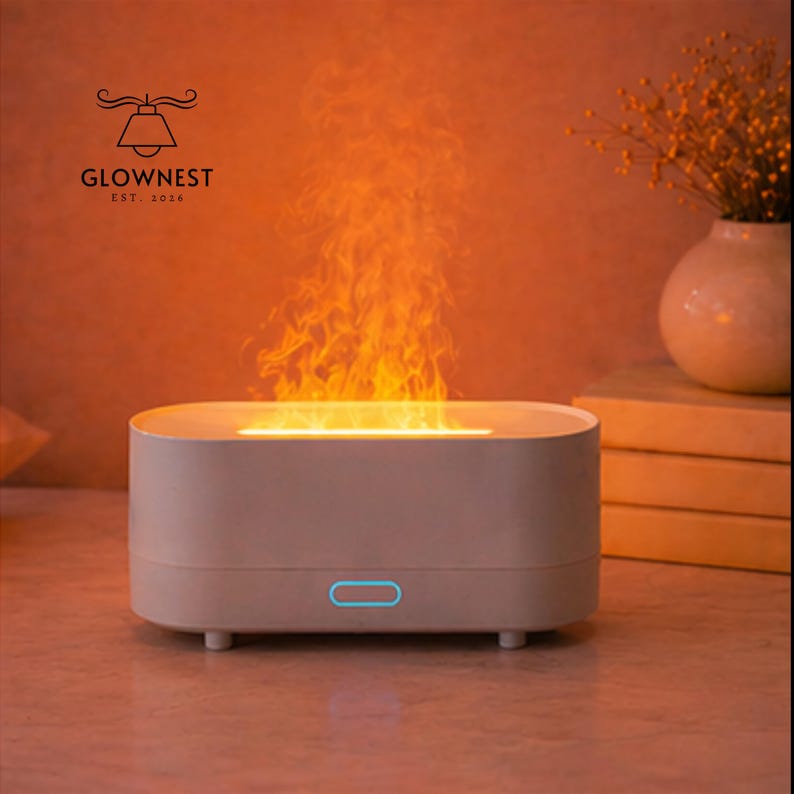 May include: An off-white aromatherapy diffuser with a flame effect. The diffuser has a blue power button and is emitting an orange flame-like vapor. The logo "GLOWNNEST EST. 2016" is visible in the upper left corner.