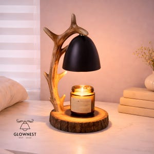 May include: A white ceramic mug with a black handle and the text "But First, Coffee" in a bold, black font. The mug is set against a blurred background, suggesting a cozy setting.