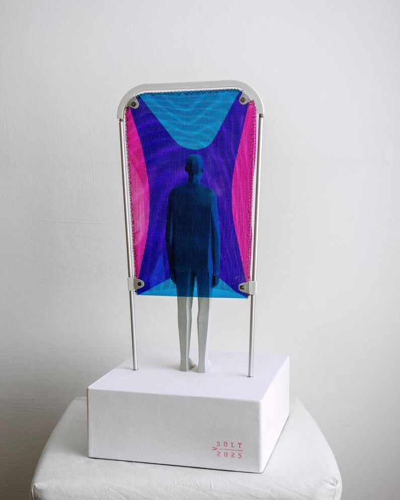 Puede incluir: Una escultura con una base rectangular blanca que tiene el texto SOLT 2025 impreso en rojo. Un marco de metal plateado sostiene una malla con patrones geom&eacute;tricos azules y rosas. Una figura humana azul se encuentra frente a la malla.