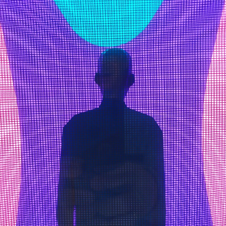 Puede incluir: La silueta de una persona se sit&uacute;a centrada frente a un vibrante patr&oacute;n de cuadr&iacute;cula retroiluminado. El fondo presenta un c&iacute;rculo cian brillante en la parte superior, que transiciona hacia tonos violeta y magenta, creando un efecto luminoso.