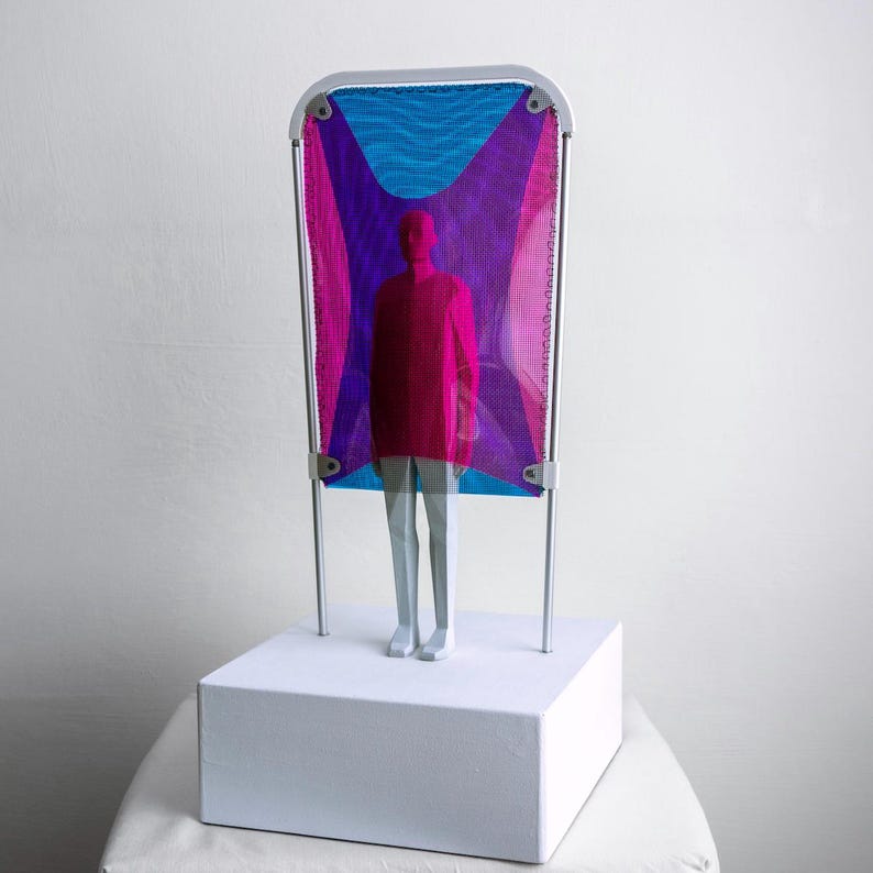Puede incluir: Una escultura que presenta una figura estilizada con top rojo y pantalones gris claro frente a un marco rectangular. El marco sostiene una malla con un patr&oacute;n vibrante de formas geom&eacute;tricas en magenta y cian, sobre una base blanca.