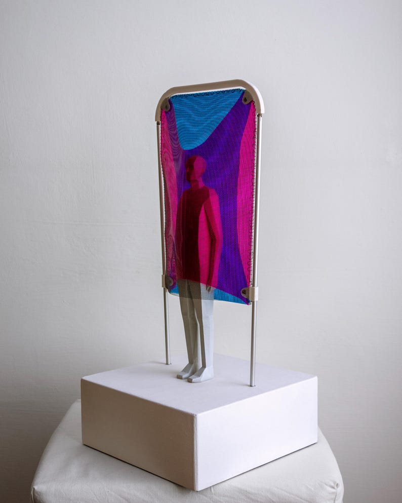 Puede incluir: Una escultura con una figura blanca de pie sobre una base rectangular blanca. Detr&aacute;s de la figura hay un marco de metal blanco que sostiene una malla transl&uacute;cida con degradados de colores azul, magenta y violeta sobre la figura.