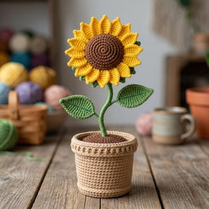 Può includere: Un girasole all'uncinetto in un vaso. Il girasole ha petali gialli, un centro marrone e foglie verdi. Il vaso è di colore marrone chiaro e presenta un design strutturato. Il fiore è esposto su una superficie di legno.