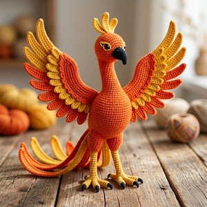 May include: A crocheted phoenix figurine featuring vibrant orange, red, and yellow yarn. The bird has outstretched wings, a crested head, a black beak, and long, flowing tail feathers. The body is crafted with a dense, textured stitch pattern.