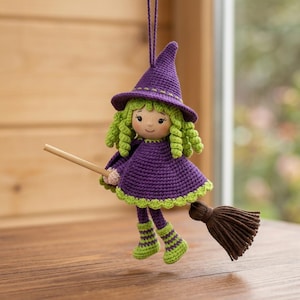 May include: A crocheted witch doll ornament featuring a purple pointed hat, a purple cape with lime green trim, and curly lime green hair. The doll wears lime green striped boots and holds a small wooden broomstick with brown bristles.
