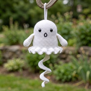 May include: A white crocheted ghost ornament featuring a rounded head, two small black bead eyes, and a stitched black mouth. The ghost has a ruffled bottom edge and a long, spiraling tail extending downward, with a loop at the top for hanging.