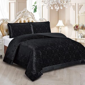 May include: A black bedspread and pillow set with a floral design. The bedding is on a bed with a decorative headboard. The room features a chandelier and a white bedside table with a lamp.
