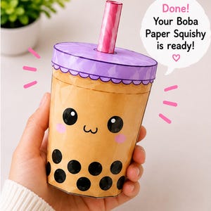 Puede incluir: Un squishy de papel de té boba con una taza color canela, una cara linda, perlas de tapioca negras, una tapa morada y una pajita rosa. Un globo de texto contiene: Done! Your Boba Paper Squishy is ready! junto a un pequeño símbolo de corazón.