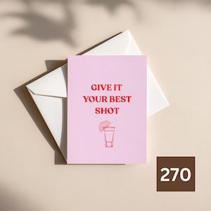 Op de afbeelding: Een lichtroze wenskaart met de rode tekst GIVE IT YOUR BEST SHOT en een rode lijntekening van een shotglas met een schijfje limoen, geplaatst op een effen witte envelop. De kaart heeft een strak en eenvoudig ontwerp.