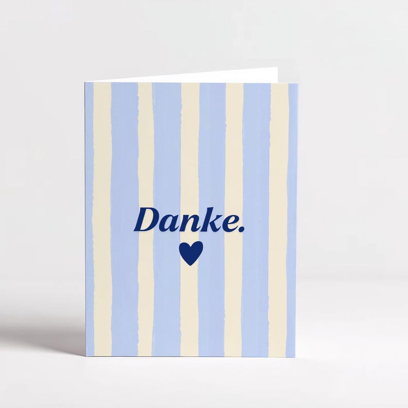 May include: A folded greeting card featuring a pattern of vertical light blue and cream stripes. The front of the card displays the word "Danke." in dark blue text, positioned directly above a small, solid dark blue heart icon.