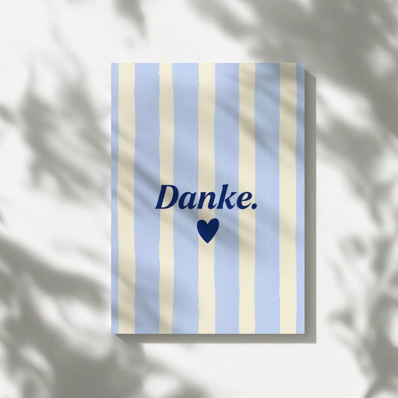 May include: A rectangular card featuring a vertical striped pattern in light blue and cream. Centered on the card is the word "Danke." written in a dark blue serif font, positioned directly above a solid dark blue heart icon.