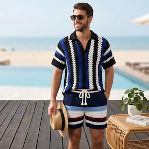 May include: A matching crochet polo shirt and shorts set in black, blue, and white stripes. The shorts have a drawstring waist. The person is holding a straw hat. The background includes a pool and beach.